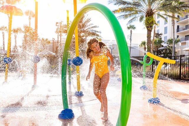 Young girl smiling while playing on the splash pad at Las Palmeras by Hilton Grand Vacations resort in Orlando. 