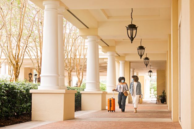Two woman walking happily into Parc Soleil® by Hilton Grand Vacations with luggage, Orlando, Florida.
