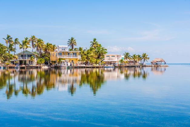 Quaint island-style homes surrounded by palm trees reflecting in calm bay waters, Key West, Florida. 