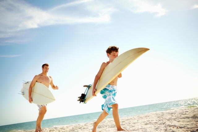 Man and young boy walking on the water's edge with surf boards, Southern California. 