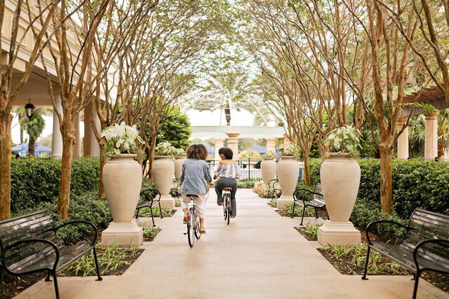 Two women riding bikes, treen covered paved bike trail, Parc Soleil, a Hilton Grand Vacations Club, Orlando, Florida. 