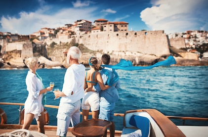 Two couples enjoying a luxury yacht sailing cruise looking at a medieval fortress on the coastline