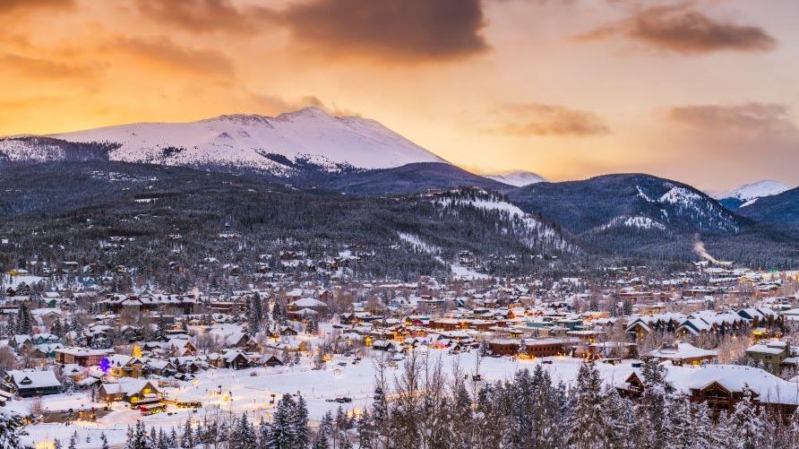 Stunning aerial image, snow-covered mountain town, snow-capped mountains in distance, cotton candy skies overhead, Breckenridge, Colorado.