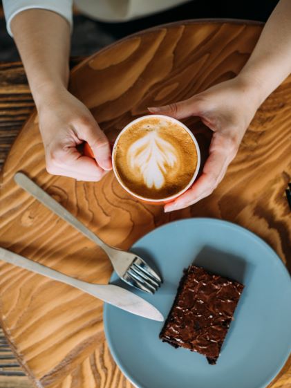 A patron at a cafe with a latte and plate with a brownie on a wooden table