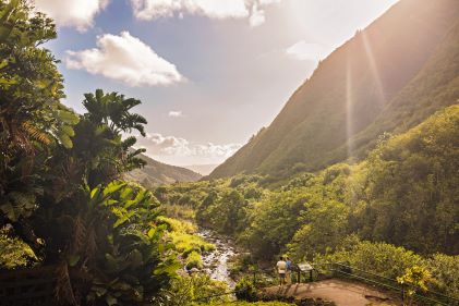 A couple admiring verdant mountain tops, blue skies, flowing creek, Iao Valley, Maui, Hawaii. 