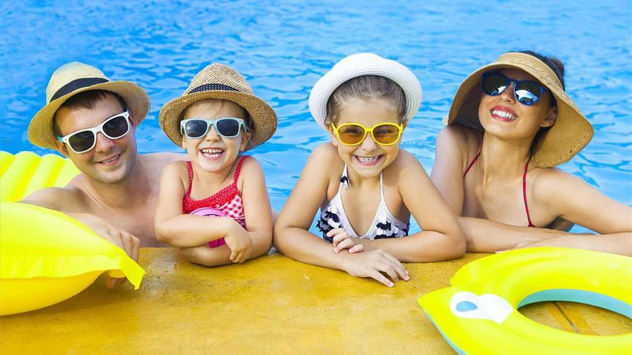 A happy family on a family vacation smiling in the pool wearing hats and sunglasses.