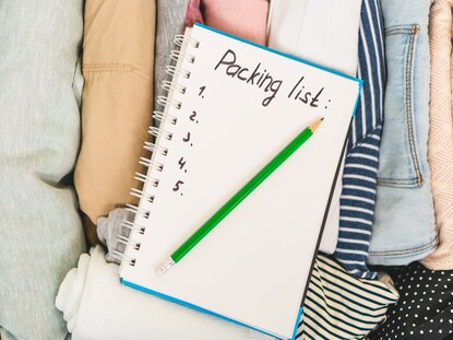 A notebook with "packing list" handwritten at the top, laid atop of clothing. 