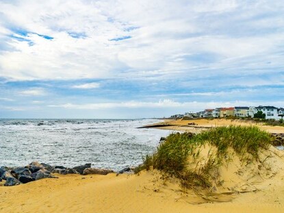 Golden sand dunes with ocean waters and quaint coastal cottages in the distance, Grommet Island Park, Virginia Beach, Virginia.